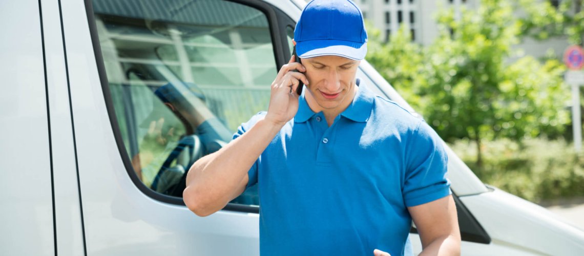 Male Worker In Front Truck Using Mobile Phone While Looking At Digital Tablet