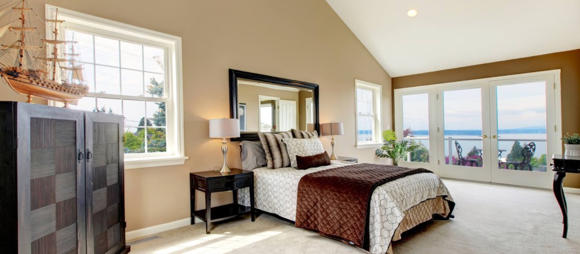 Beige classic large bedroom with water view and carpet.